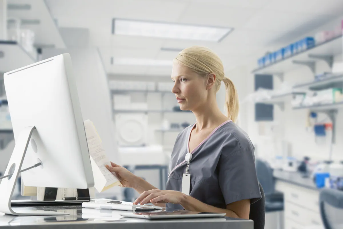 Healthcare professional reviewing documents on a computer for medical coding outsourcing.