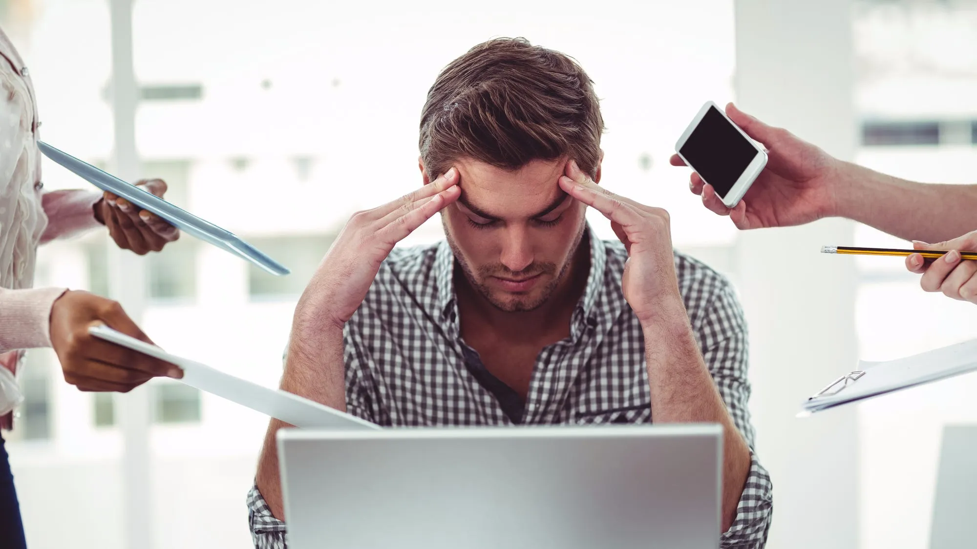 Stressed man at desk surrounded by documents, phone, and pencil, showing stress and pressure at work.